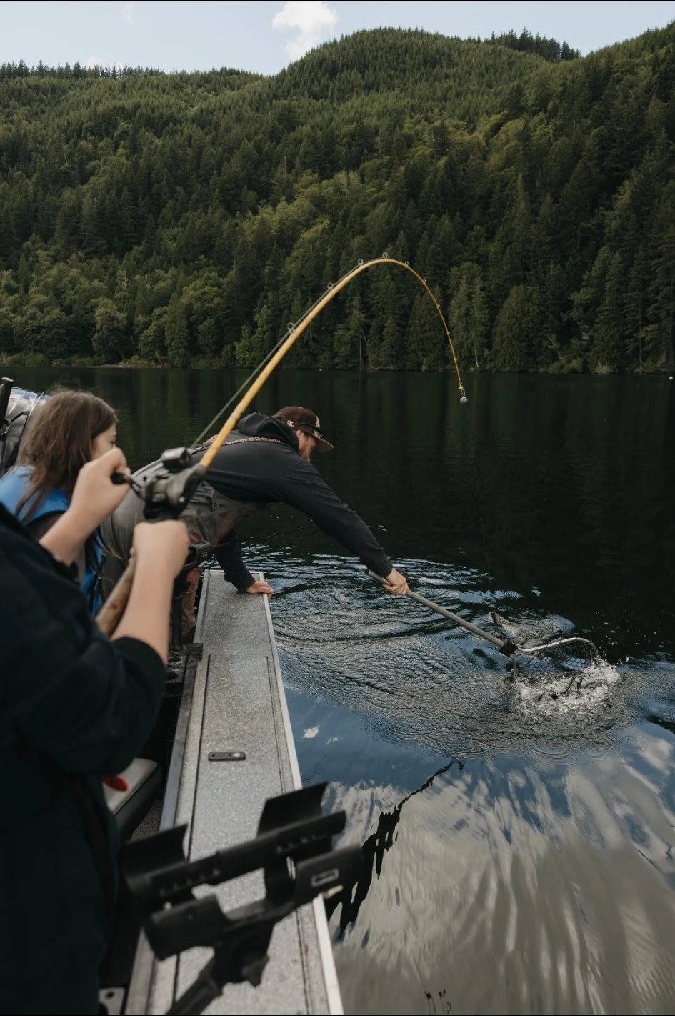 Youth reeling in a fish while an instructor helps with the net